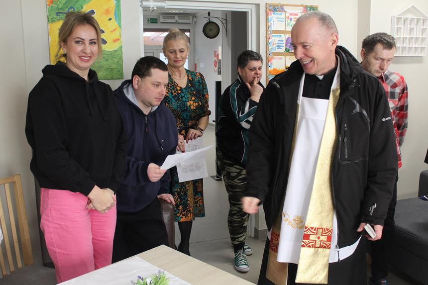1.Uśmiechający się ksiądz na tle uczestników oraz kadry D