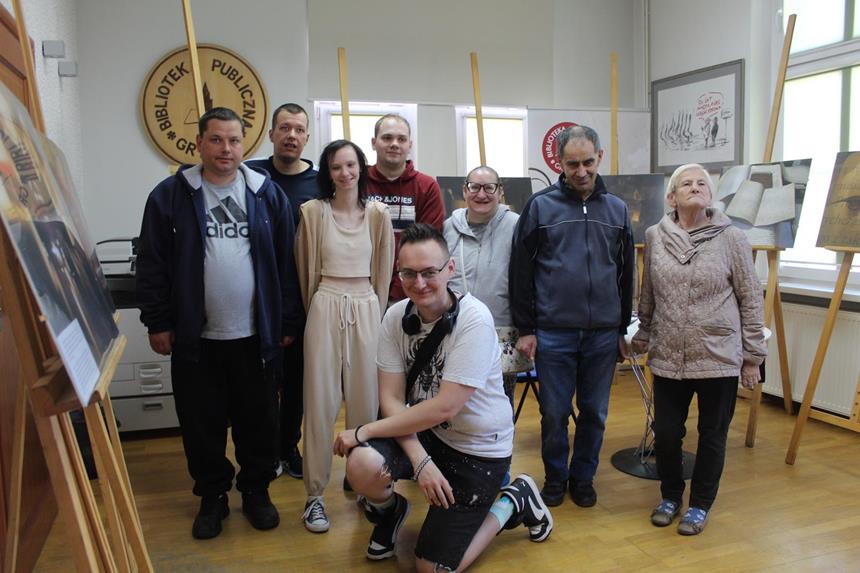 Fotograf oraz grupa uczestników stojący na tle wyeksponowanych fotografii 