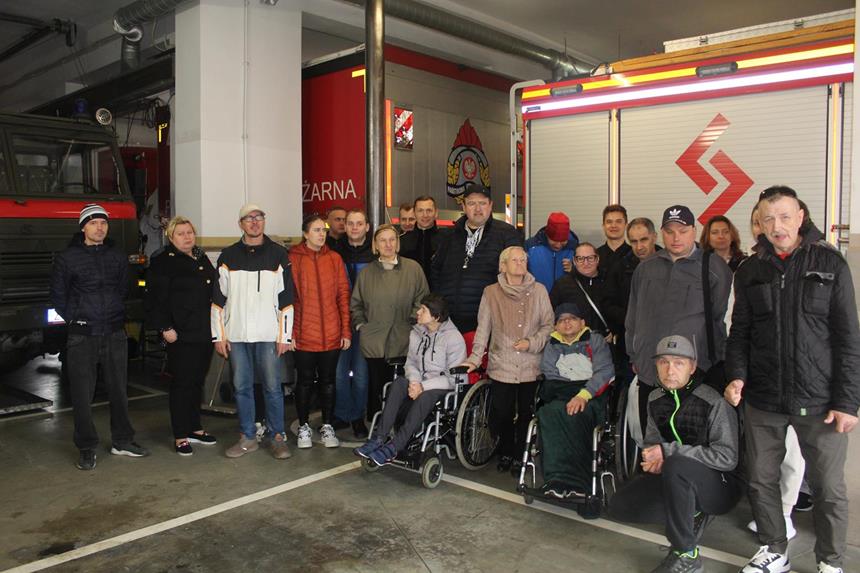 Grupa uczestników oraz strażaków stojąca na tle wozów strażackich 
