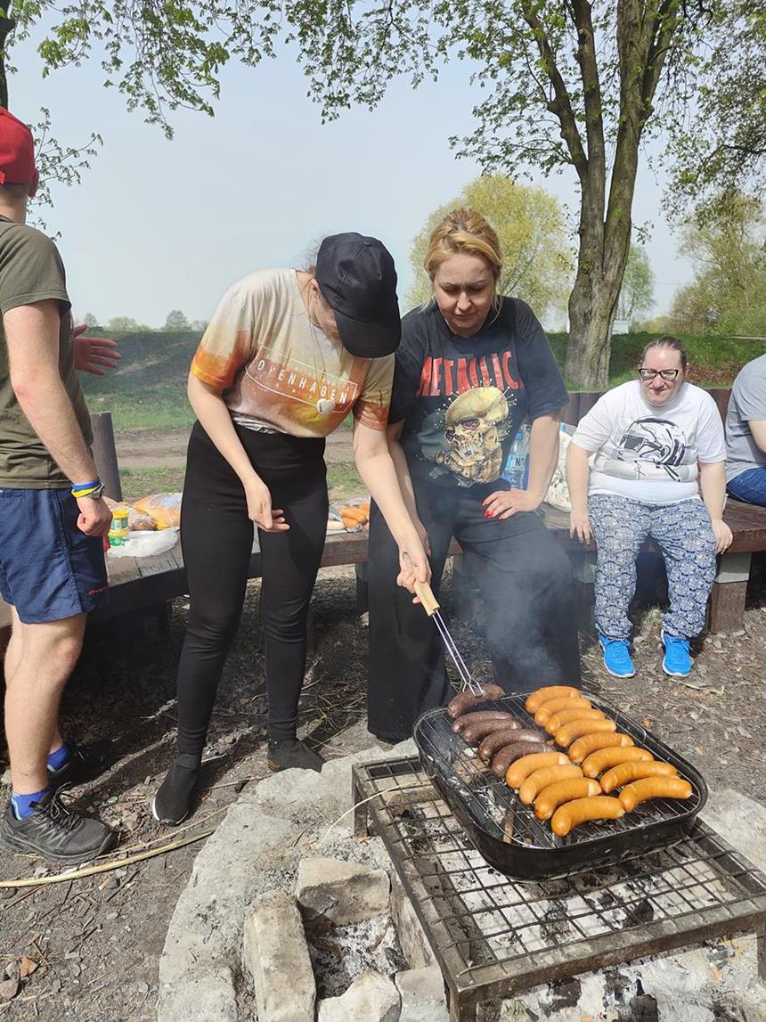 Uczestniczka i terapeutka grillujący kiełbaski na tle drzew 