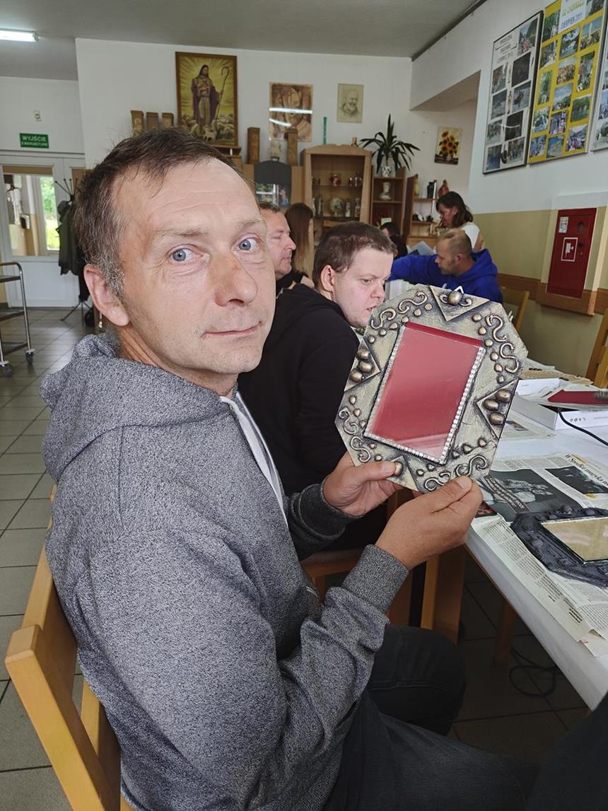Uczestnik w szarej bluzie prezentujący wykonaną własnoręcznie ramkę na zdjęcia 