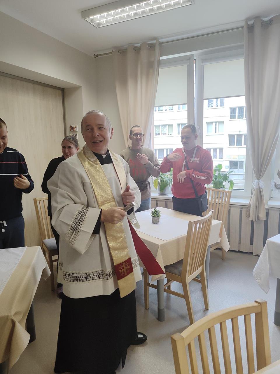 1.Ksiądz trzymający kropidło na tle modlących się osób D