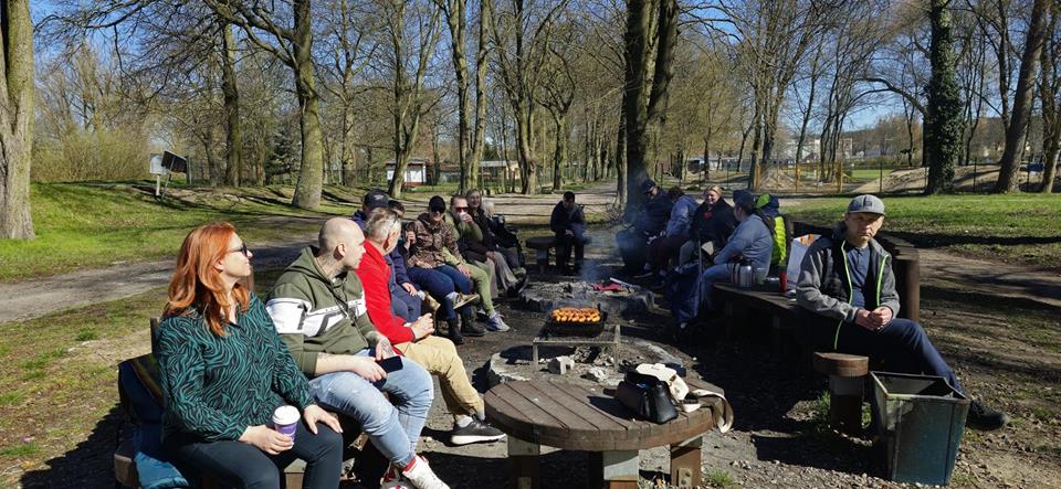 Uczestnicy siedzący na drewnianych ławkach przy grillu