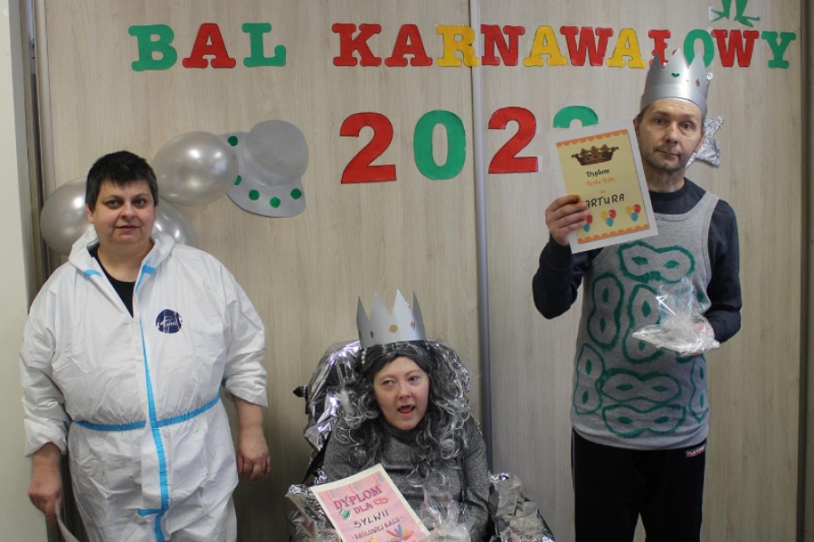 8 – Uczestniczka pozuje do zdjęcia z Królem oraz Królową balu na tle napisu. 