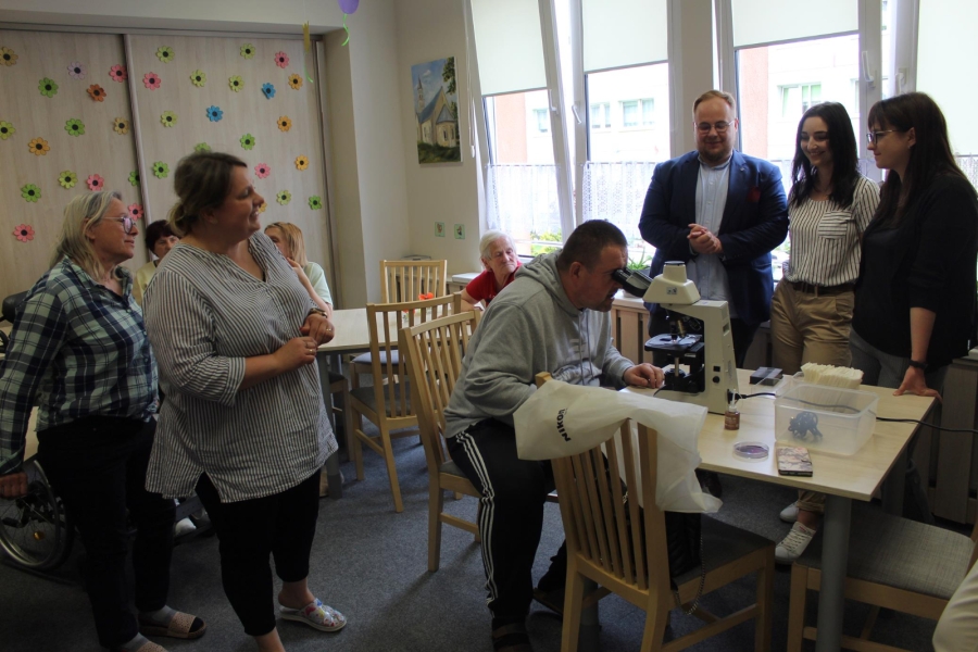 Uczestnik patrzy w mikroskop na tle gości oraz Uczestników.