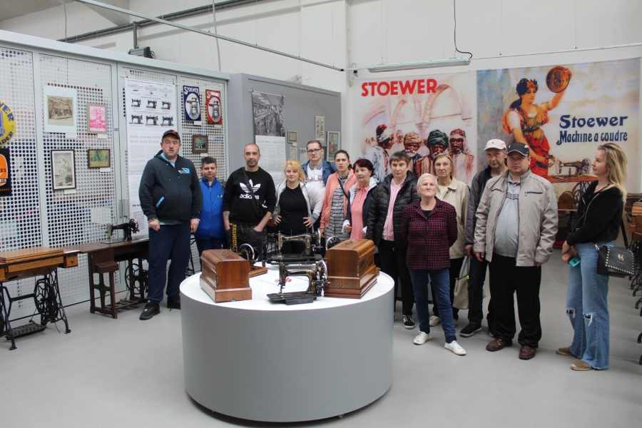 Uczestnicy pozujący do zdjęcia grupowego na tle ekspozycji maszyn do szycia.