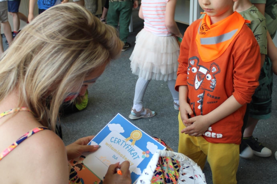 Pani pedagog wypisująca chłopcu dyplom na tle grupy.