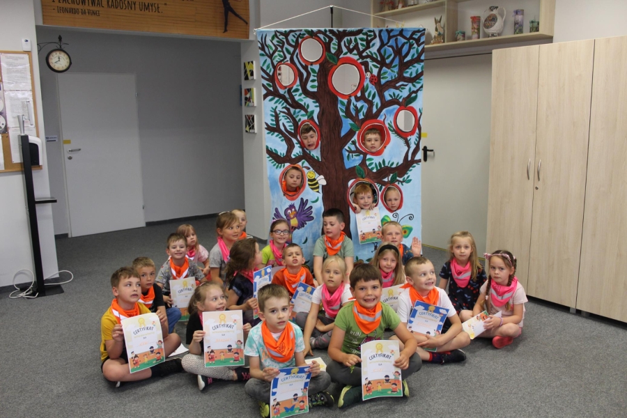 Grupa dzieci trzymająca dyplomy pozuje do zdjęcia siedząc. 