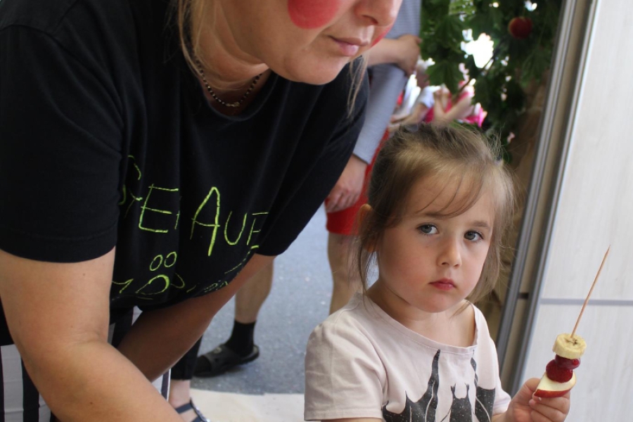 Dziewczynka wraz z terapeutą nawleka owoce na drewniane patyczki.