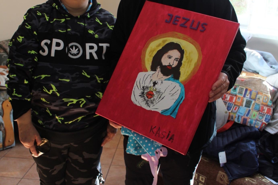 9. Ksiądz trzymający w dłoni obraz namalowany przez Uczestniczkę pozuje do zdjęcia.