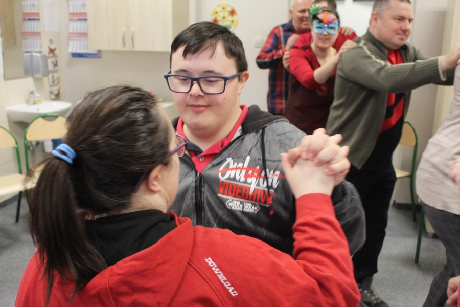 5.Uczestnik i Uczestniczka tańczący trzymając się za ręce na tle bawiącej się grupy