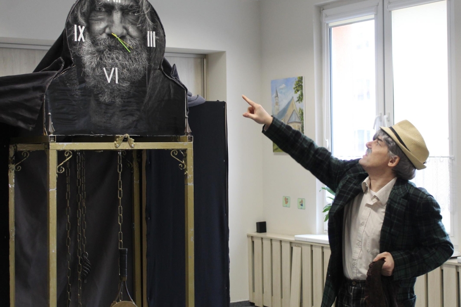 1.Aktor w kapeluszu wskazujący palcem na zegar z nadrukiem starca