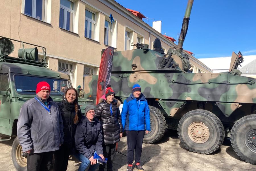 5. Grupa uczestników pozująca do zdjęcia na tle pojazdu opancerzonego