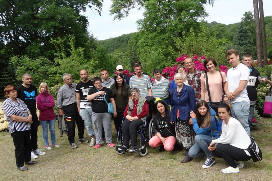 Zdjęcie grupowe uczestników oraz terapeutów na tle ogrodu dendrologicznego