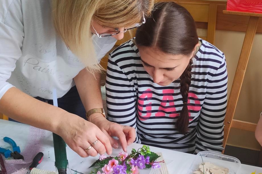 4.Terapeutka oraz uczestniczka przyklejające kwiatki do drewnianej ramki