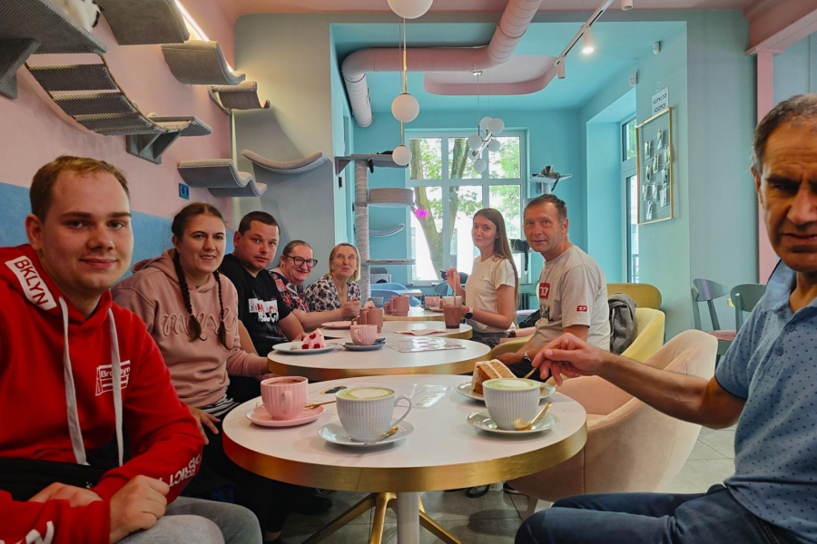 1.Uczestnicy oraz Fizjoterapeuta siedzący przy okrągłych stolikach przy kawie i ciastku