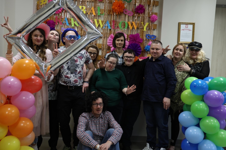 1.Uczestnicy oraz kadra w strojach karnawałowych na tle złotych serpentyn i kolorowych balonów