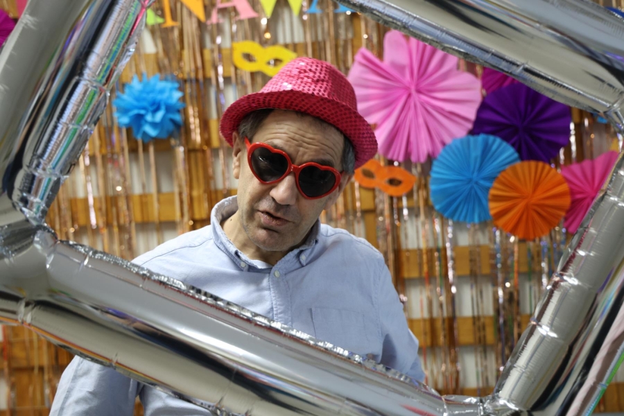 5.Uczestnik w kapeluszu oraz okularach na tle kolorowych ozdób oraz dmuchanej ramki