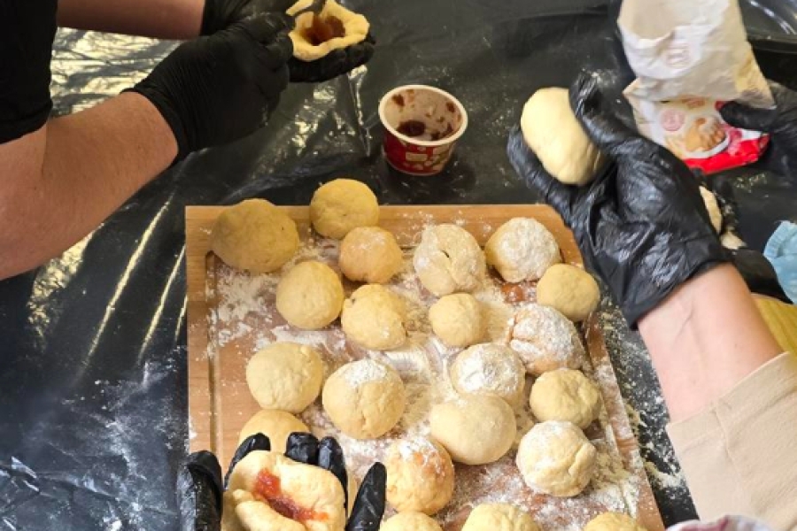 2.Uczestniczka nadziewająca pączka na tle wyrobionych pączków