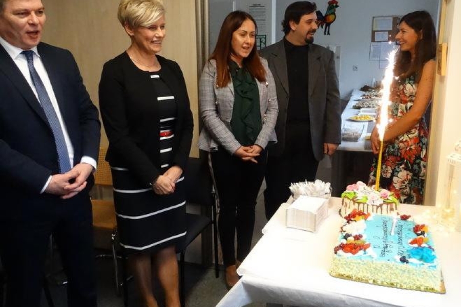 Uczestnicy, goście oraz terapeuci na tle tortu z palącą się świeczką