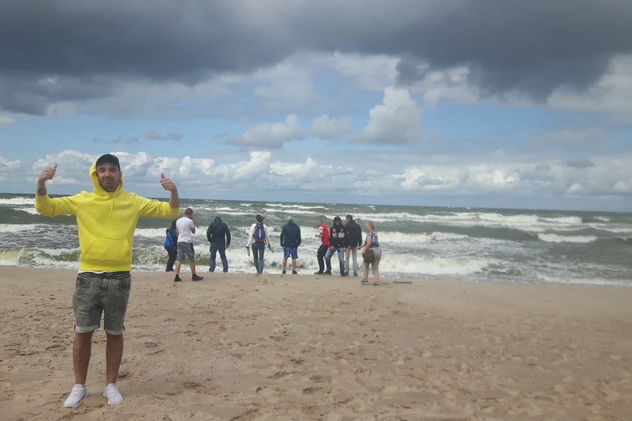 Uczestnik pozujący do zdjęcia na tle całej grupy zwróconej ku morzu.