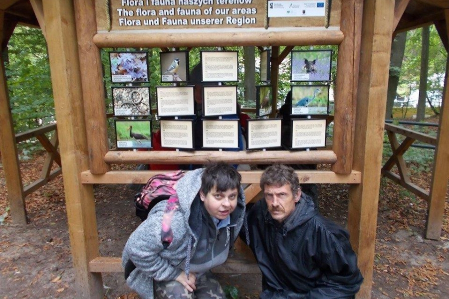 Dwójka uczestników na tle tablicy informacyjnej w puszczy bukowej