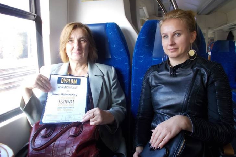 Uczestniczka chwaląca się dyplomem w obecności pedagoga w pociągu