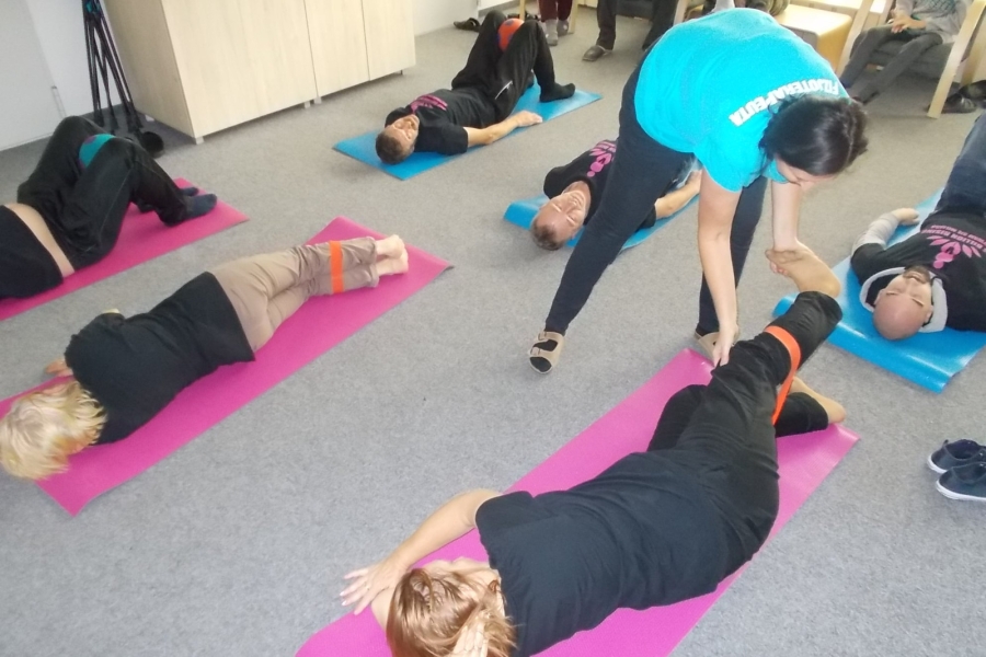 Uczestnicy leżący bokiem na karimatach wykonujący ćwiczenia z gumą