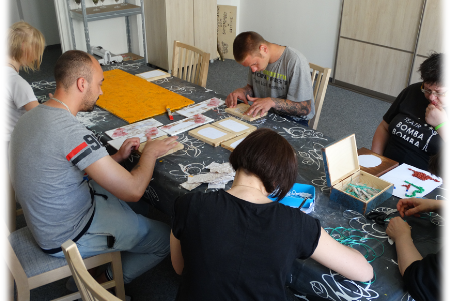 Grupa uczestników pochylona nad swoimi pracami z drewna i papieru.