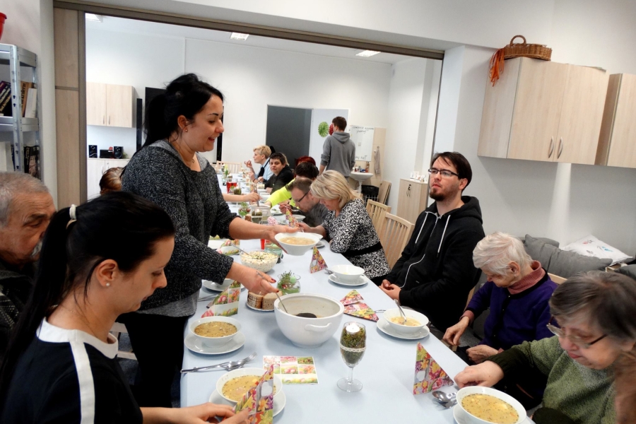 Stół przy, którym siedzą uczestnicy a przy nim terapeutka nalewając zupę do talerza.