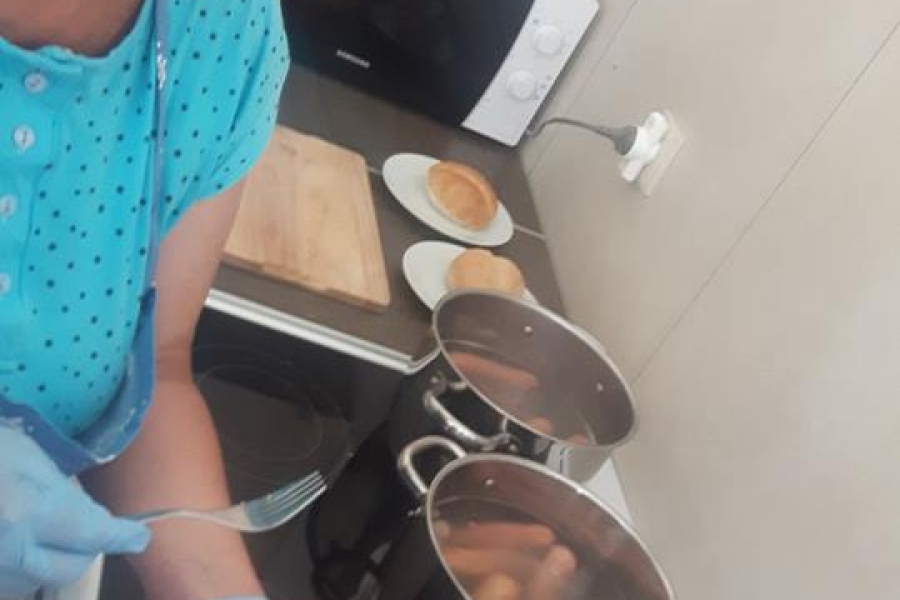 Uczestniczka podaje w bułce ugotowane kiełbaski, które są polewane ketchupem.