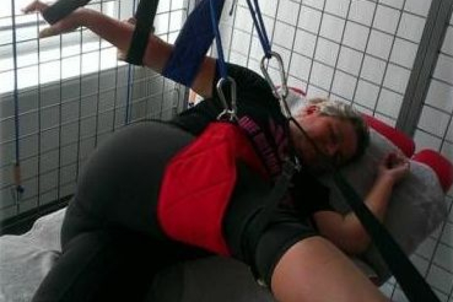 Leżąca uczestniczka ćwicząca na podwieszkach rękę i nogę.