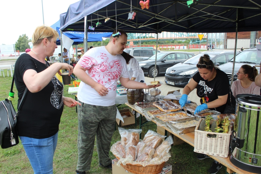 3 – Pracownik ŚDS w Gryfinie nakładający ciasto na tle pikniku.