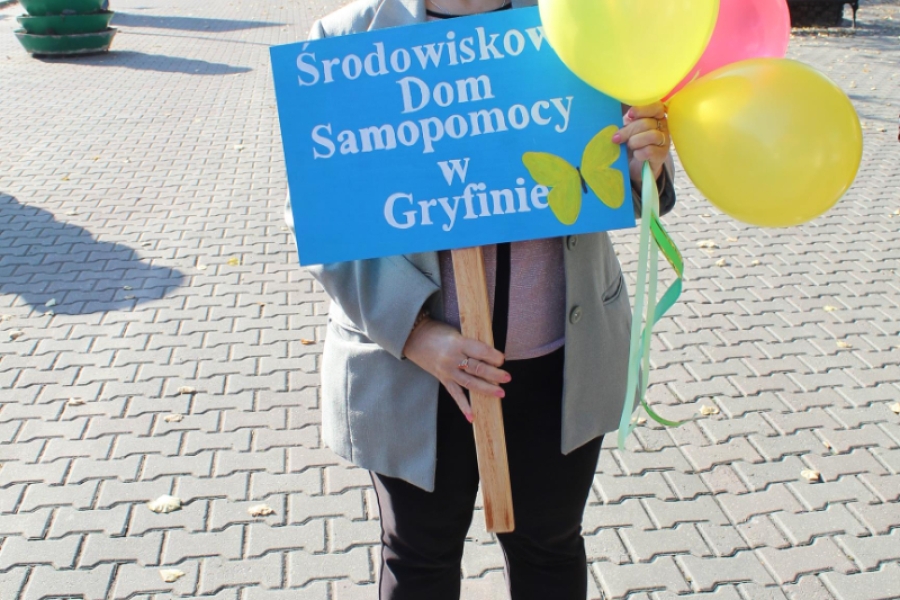 4 – Uśmiechnięta Uczestniczka trzymająca transparent oraz kolorowe balony.